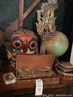 Photo shows large colorful ceramic owl statue, vintage globe, wooden carved figure resembling a ship, open wooden box with multiple metal paint containers, and small decorated tin box