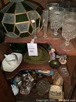 Photo of multi-faceted retro lampshade and clear vintage drinking glasses on shelf with assorted items below