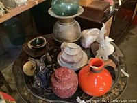 Overall assortment of Bavarian plates, English china cups, various figurines, an orange ceramic pot with chipped rim, and the red resin lacquer urn along with a green glass sphere on a metal base.