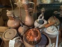 Image showing various copper pots and kettles arranged closely on a surface, some with lids and wooden handles, in used condition.