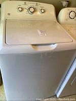 Front view of white GE top load washing machine with closed lid and control panel visible