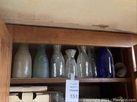 Wooden shelf containing seven vintage milk glass bottles in white, blue, and clear glass.