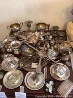 Overhead view showing assortment of sterling silver items including sugar bowls, candlesticks, salt and pepper shakers, gravy boat, tongs and plates on table