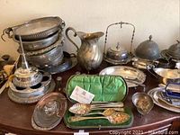 Overview of stacked pierced bowls, pitcher, lidded baskets, green velvet servers and assorted pieces