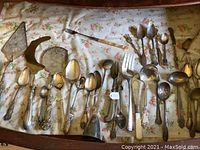 Top-down view of assorted silver-plated spoons, forks and serving utensils on floral cloth lining