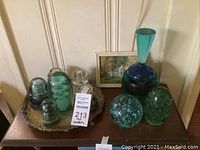 Image showing a collection of turquoise glass insulators and a small framed landscape painting on a wooden table.