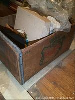 Wooden box containing a variety of textiles including scarves and fabrics inside a plastic bag.
