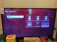 Full front view of TCL Roku TV showing active home screen with HDMI and AV inputs visible, with remote control likely nearby.