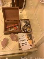 Wide shot showing costume jewelry pieces in wooden and cardboard boxes plus two pink stone elephant figurines on the left.