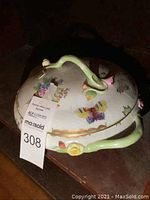 Side angle showing floral and butterfly decorations on lid and body, with curved green handles and flower accents.
