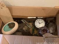 Top view of open cardboard box showing vintage metal keyhole covers, turn key parts, clock, and other small decorative hardware items