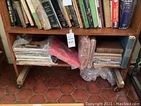 Wide view of lower shelf showing several plastic-wrapped hardcover books and stacked magazines