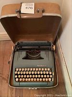 Photo of vintage Smith Corona typewriter inside beige hard case, showing keyboard, case interior, and part of the exterior case