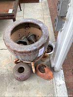 Top view of large ceramic planter on wooden stand showing metal funnels and gardening tools inside, with smaller purple and terracotta planters beside it.