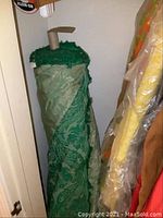 Large bolt of heavy green floral patterned fabric with a rod inserted in the center, positioned vertically in a small closet space.