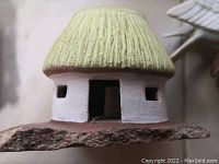 Close-up photo of ceramic African house with thatched roof, white walls, small windows and open door.