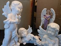 Image showing white porcelain angel and cherub sculptures in front and painted polystone angel figurine in background