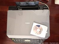 Top view of gray Canon office jet multifunction device with control panel and installation CD on top