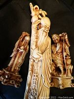 Front view of three polystone figurines showing detailed carved longevity figures in ivory and brown tones