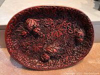 Top view of the snack holder showing intricate raised grape and leaf pattern in reddish lacquered style.