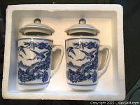 Two Chinese porcelain tea mugs with lids in molded white styrofoam packaging.