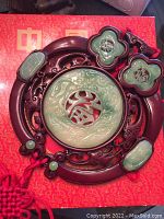 Close-up of circular Chinese wall decoration showing intricate jade-style carvings and red braided tassel.