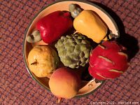 Top-down photo showing the ceramic fruit display bowl containing six colorful ceramic fruits including bell peppers, artichoke, peach, quince, and dragon fruit.