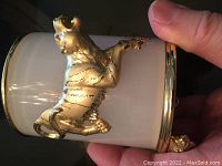 Close-up of glass pen holder showing golden tiger figure decoration and cylindrical shape with gold trim.