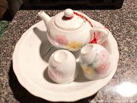 Miniature ceramic tea set showing teapot, cups, and plate from different angles