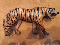 Side view of tan paper mache tiger sculpture with black stripes and open mouth showing teeth