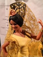 Close-up of large flamenco dancer doll's head and upper body, showing black hair, orange flower, and yellow lace head covering