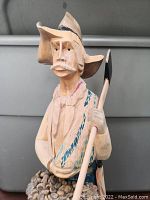 Front view of wood carved farmer holding a stick, detailed facial features, painted clothes and hat.