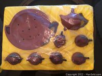 Photo of unopened Chinese earthenware tea set consisting of a teapot, six tea cups, and a drainage tray in yellow padded packaging with plastic wrap.