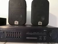 Front view of Yamaha amplifier with two JBL speakers on top. Shows brand and model details.