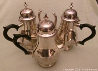 Three silver-plated coffee serving pots with black plastic handles, pear-shaped bodies, and hinged lids with finials, showing wear and tarnish.