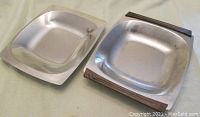 Both mid century modern square stainless steel serving dishes shown together, one with faux wood handles and the other all stainless steel.