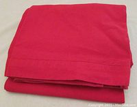 Folded red fabric tablecloth showing solid color and stitching details.