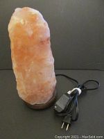 Front view of Himalayan salt lamp showing natural salt crystal on wooden base with black power cord and plug.