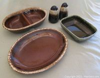 Four drip glaze ceramic serving pieces: a brown oval platter, a brown oval divided bowl, a green rectangular bowl/planter, and a pair of dark lava drip salt and pepper shakers without stoppers, shown from top and side view on neutral background.