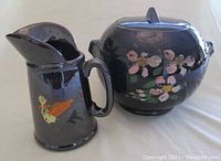 Photo of two black ceramic items: a batter pitcher with painted bird and a cookie jar with floral decoration