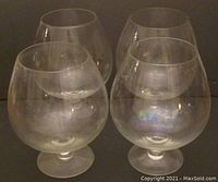 Four clear oversized snifter glasses arranged in a group, showing their similar shape and size.
