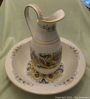 Pitcher placed inside basin showing the full set with multicolored painted serpent, floral, and scroll decoration on white ceramic.