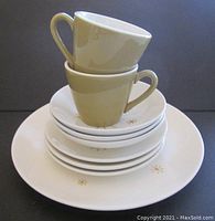Stacked view showing two beige coffee cups placed on top of a pile of saucers and dinnerware, highlighting item count and condition details visible.