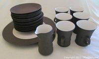 Lot composition showing stacked plates, coffee cups, creamer jug in matte brown finish with smooth white interiors.