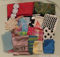Grouped display of approximately 18 vintage scarves showing various designs and colors including solid red, polka dot, floral appliques, and peacock feather print