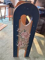 Close-up of one side of the wooden quilt rack showing the painted floral decoration and the curved shape of the rack end.