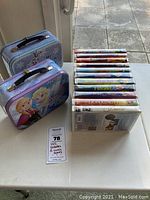 Photo showing two metal Frozen-themed lunch boxes and 10 Disney VHS tapes arranged upright with spines visible