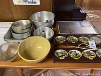 Overview of warming trays including large Salton metal warming tray and smaller Currier & Ives design warming trays along with assorted vintage kitchenware like metal bowls, pot, cake pans, and large yellow ceramic bowl