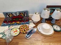 Photo of rug hooking art, lamps, dishware, crocheted pieces, small decorative plate, and electric knife showing lot variety