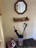 View of octagonal wood-framed mirror and wooden shelf on wall above umbrella stand and snowman flag on floor.